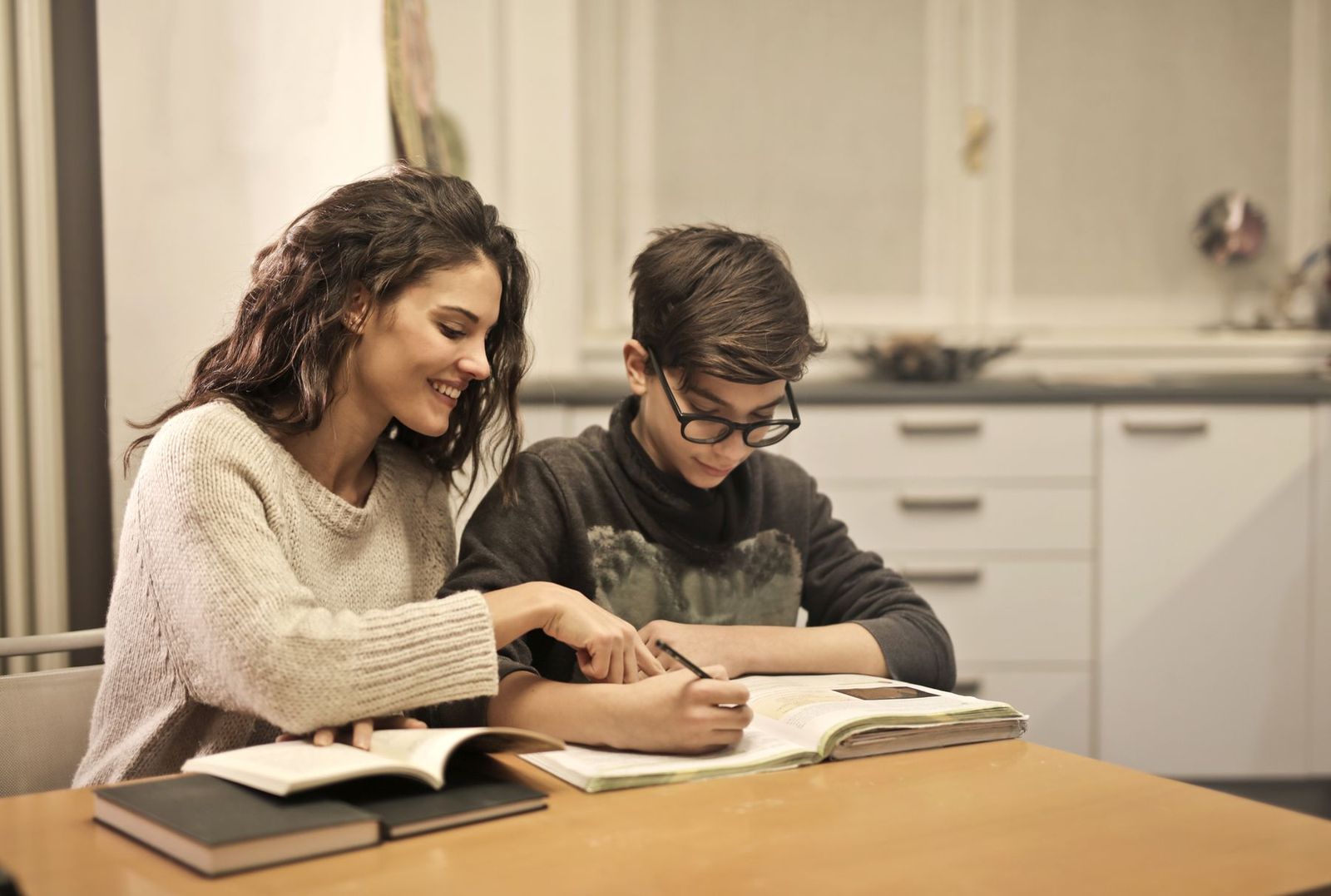 Junge Frau hilft ihrem jüngeren Bruder am Tisch mit Büchern bei den Hausaufgaben